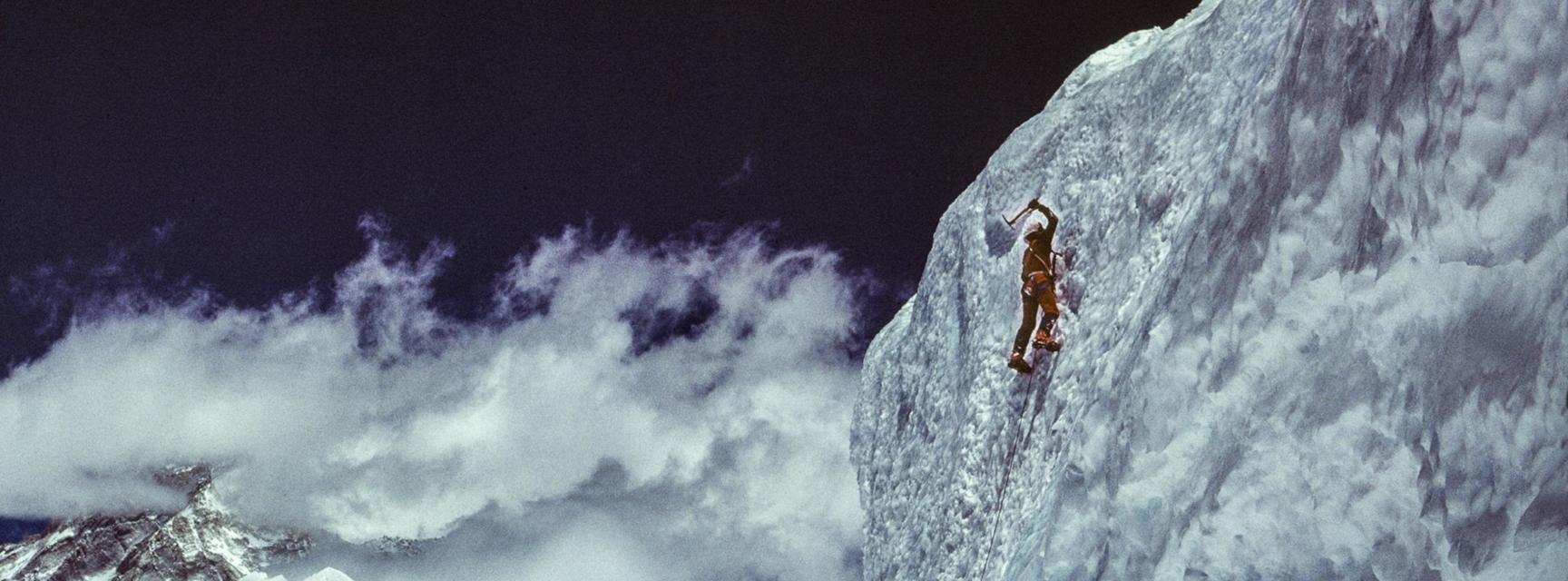 Mountain climber on a sheer face with range and clouds in background
