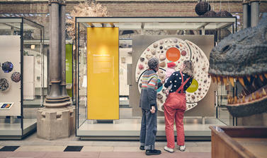 3 generations of a family looking at a display with the model of a T.rex head on the right.