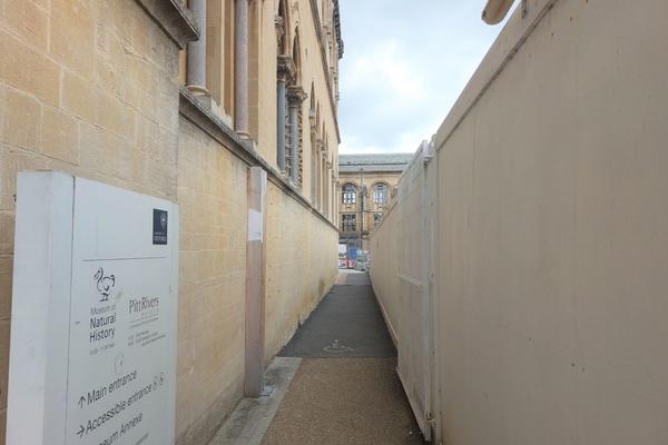 A view of the path to the accessible entrance. The path is between the outside of the building and some barriers called hoarding.