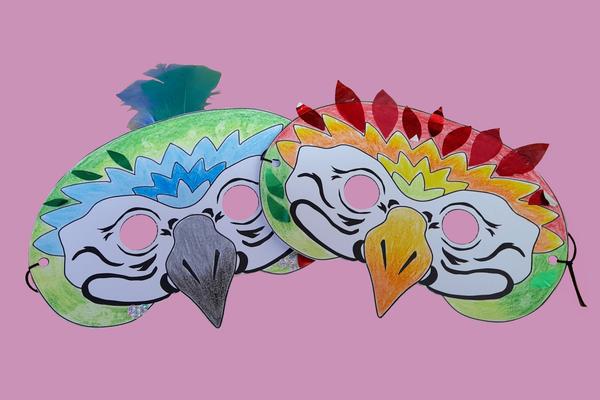 Two completed macaw mask crafts decorated with feathers and coloured in
