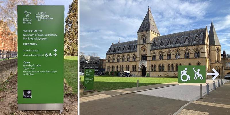Exterior view of the Oxford University Museum of Natural History building with a green directional sign in the foreground showing wheelchair and stroller symbols pointing toward the accessible entrance.