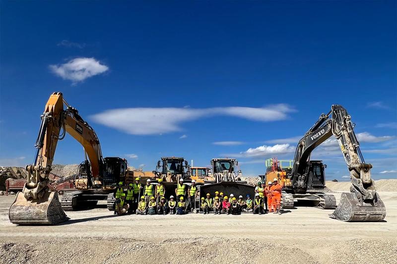 Excavation team posing in front of large construction machinery including excavators and loaders at a quarry site under a clear blue sky. Excavation team posing in front of large construction machinery including excavators and loaders at a quarry site under a clear blue sky.