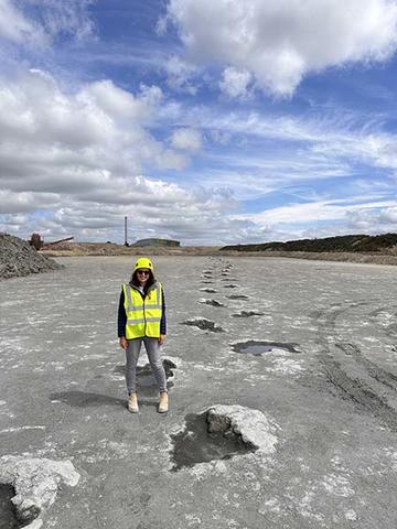 Professor Kirsty Edgar in hi-viz jacket standing beside a trail of sauropod footprints leading into the distance