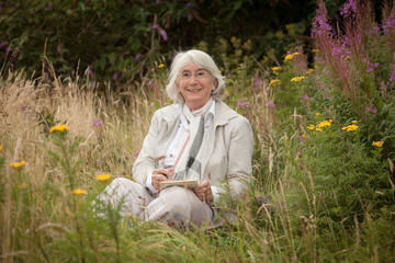 Dr Sarah Watkinson writing poetry in a meadow